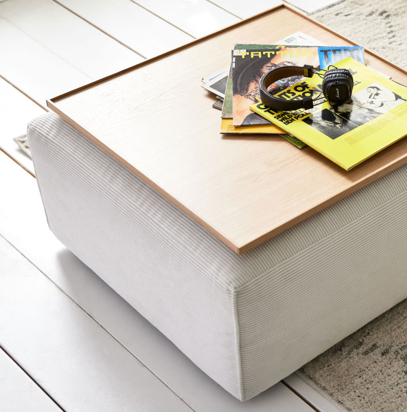 Ein Holztablett mit Zeitschriften und Kopfhörern auf einem gepolsterten Roomio-Hocker, platziert auf einem hellen Holzboden.