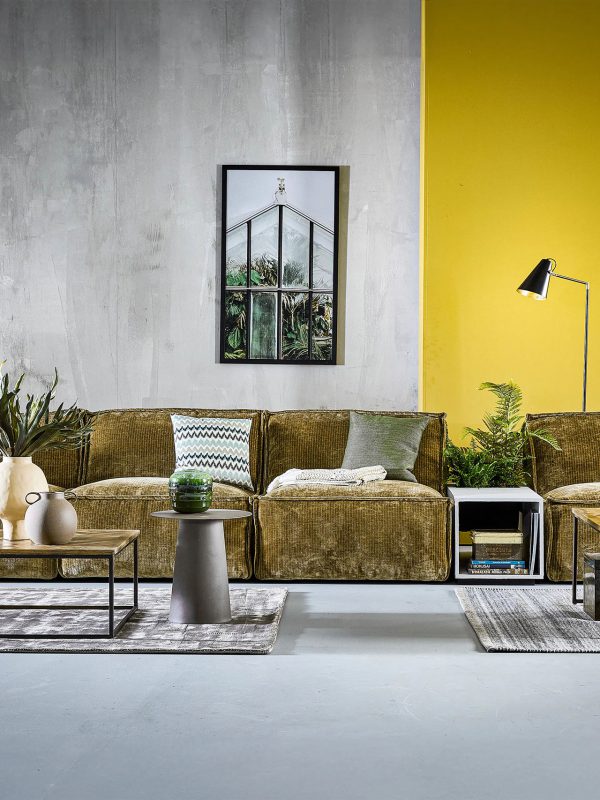 Modernes Wohnzimmer mit großem olivgrünem Sofa, gelber Akzentwand, Couchtischen und Topfpflanzen.