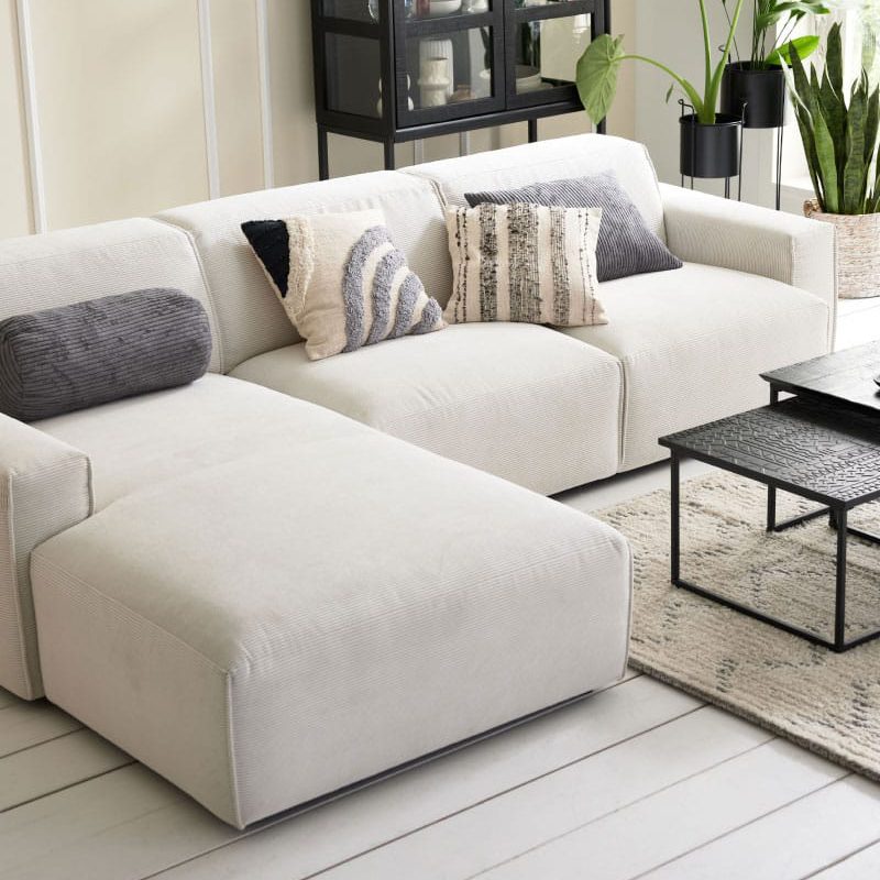 Modernes Wohnzimmer mit einem weißen Sofa, einem schwarzen Couchtisch, einer großen Pflanze und einem Schrank.